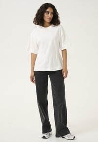 Witte katoenen t-shirt met korte mouwen, gecombineerd met zwarte high-waisted wijde jeans. Schoenen zijn wit met grijze accenten.