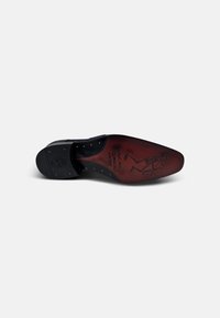 Suela de zapato de cuero negro con plantilla roja, que presenta un gráfico de esqueleto de dibujo animado y pequeños tachuelas cónicas para agarre. Forma plana y redondeada.