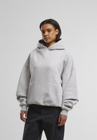 Hellgrauer, übergroßer Hoodie mit einer Fronttasche und verstellbarem Kapuzenzug. Er verfügt über gerippte Bündchen und einen gerippten Saum und ist aus weichem Baumwoll-Mischgewebe gefertigt.