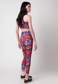 Vícebarevná sportovní podprsenka a legíny s nápadným vzorem ovoce v červené, fialové a černé; hladká látka; těsné přilnutí; atletický styl.