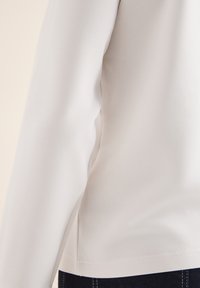 Witte langemouwen top van zachte stof, met een zijsplitontwerp en een gladde textuur, gecombineerd met donkere denim jeans.