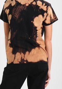 Black and tan tie-dye t-shirt, short sleeves, soft fabric, abstract pattern with varying circular and irregular shapes on the back side.