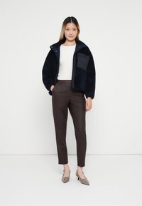 Sötétkék fleece dzseki cipzárral, mellzsebbel, barna szabott nadrággal és taupe magassarkú cipővel párosítva.