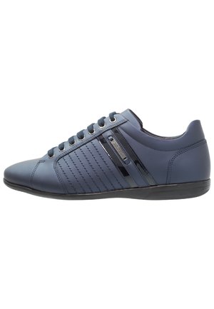 Dunkelblauer Low-Top-Sneaker mit Schnürung vorne, genähten Seitenstreifen und glänzendem schwarzen Akzent auf einer flachen schwarzen Sohle.
