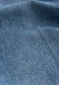Close-up van blauwe denimstof met diagonale keperbinding en lichte plooien in het materiaal.