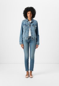 Jachetă din denim de culoare albastru deschis, cu nasturi, două buzunare pe piept și spate simplu. Asortată cu blugi albaștri deschiși, ajustați și balerini roz simpli.