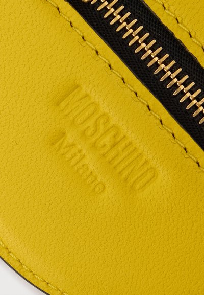Κίτρινο δέρμα με υφή και ανάγλυφο λογότυπο "MOSCHINO Milano" και χρυστό φερμουάρ ραμμένο με μαύρη υφασμάτινη ταινία.