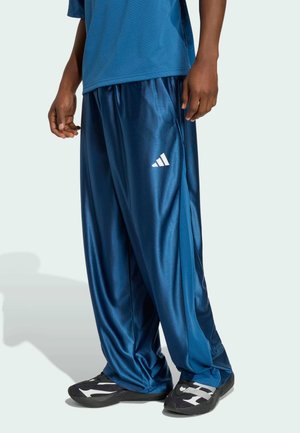 Blå satin træningsbukser med løs pasform, med en hvid Adidas-logo på venstre side og en glat, skinnende tekstur.