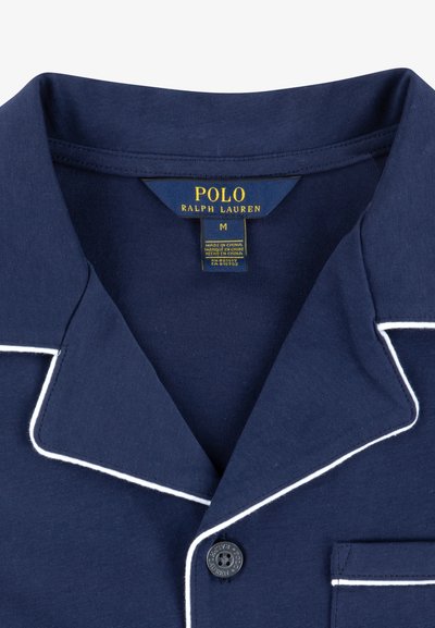 Cămașă de noapte din bumbac bleu marin cu detalii albe, având guler tip notch, un mic buzunar la piept și un nasture negru inscripționat cu "POLO". Mărimea M.