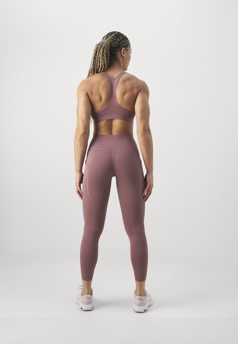 Bra sportivo e leggings in un colore rosa tenue, con design a schiena scoperta, texture liscia e tasche laterali sui leggings.