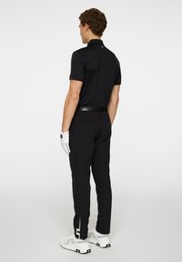 Črna polo majica s kratkimi rokavi, slim-fit hlače, bele golf rokavice in teniske s vzorcem. Ima pravilen ovratnik in eleganten dizajn.