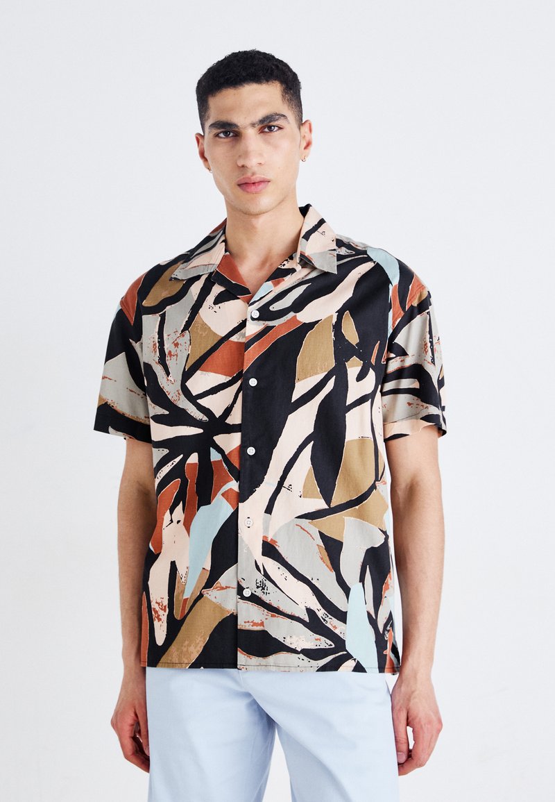 Chemise à manches courtes avec boutons, présentant un motif abstrait multicolore, avec des accents beige, noir et pastel sur un tissu léger.