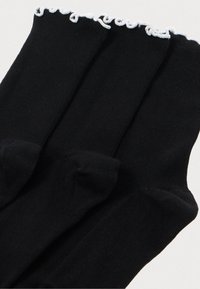 Mustad mustrid sokid mustast puuvillast, millel on soonikkoes ja valge pitsiosa äärmisel, kokkupandult.