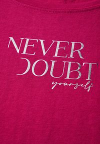 Chemise en coton fuchsia avec texte réfléchissant argenté "NE JAMAIS DOUTER de vous-même", dotée d'un col rond et d'une texture côtelée.