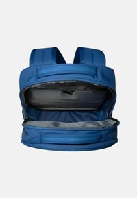 Modrý batoh s dvěma polstrovanými ramenními popruhy, hlavním oddílem na zip a měkkou šedou podšívkou. Má elegantní plochý design.