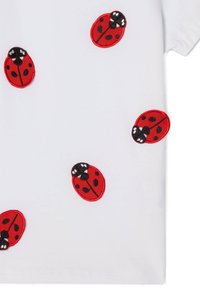 Hvid skjorte med røde broderede mariehøne-designs, der har sorte pletter og ansigtstræk, spredt over stoffet.