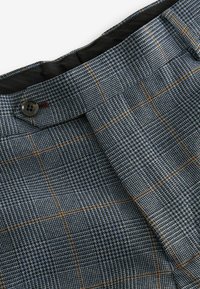 Textured blue checkered trousers featuring a mix of houndstooth and line patterns, with a prominent button at the waistband.