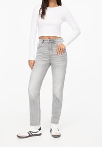 Jean gris taille haute avec une coupe droite, associé à un crop top blanc à manches longues et des baskets blanches avec des accents noirs.