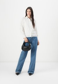 White eyelet button-up shirt with long sleeves, paired with light blue wide-leg jeans. Holds a small black handbag with a knotted handle.