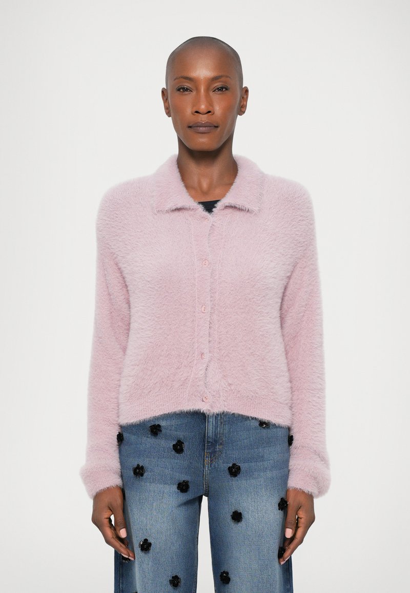 Svetloružový nadýchaný kardigán s golierom a zapínaním na gombík, s krátkym strihom. Skombinovaný s modrými džínsami zdobenými čiernymi kvetinovými aplikáciami.