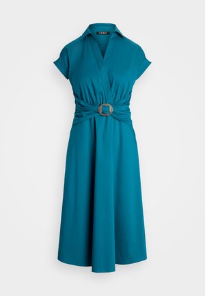 Rochie turcoaz, cu design înfășurat, mâneci scurte, talie strânsă și un accent cu cataramă pătrată de nuanță argintie. Textură de stofă netedă.