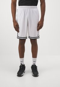 Balti sportiniai šortai su juodomis šoninėmis juostelėmis ir juodu Nike logotipu, elastinga juosmens juosta, kvėpuojanti tinklinė medžiaga, derinami su juodais batais ir baltais kojinėmis.