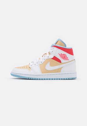 Baskets montantes en cuir blanc perforé, panneaux beige, maille rouge près de la cheville, semelle et doublure bleues, et logo Air Jordan rouge sur le côté.