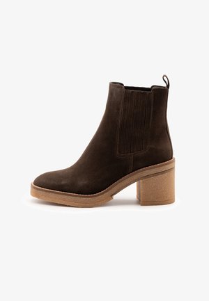 Stivale alla caviglia in suede marrone scuro con pannelli elastici laterali, un anello sul retro e tacco e suola in gomma bloccata beige.