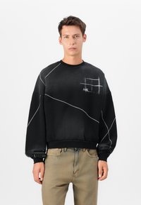 Schwarzer Sweatshirt mit diagonalen weißen Nähten, rundem Halsausschnitt und einer Brusttasche. Das Material sieht weich und strukturiert aus.