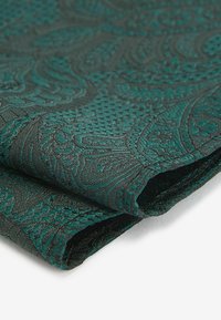 Tissu bleu canard avec des motifs paisley complexes, présentant une surface texturée et des bords pliés, mettant en valeur un savoir-faire de qualité.
