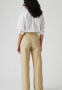 Beige hoge taille broeken met een rechte snit, voorzien van dubbele achterzakken en een gladde textuur, gecombineerd met een wit shirt.