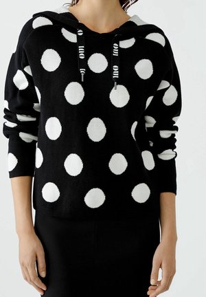 Sweatshirt noir à pois blancs, avec capuche, cordons de serrage et manches longues. Texture douce, design décontracté et coupe confortable.