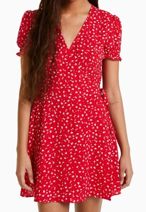 Vestido rojo con flores, mangas cortas abullonadas, escote en V y cintura ajustada. La tela presenta patrones florales blancos y una falda fluida.