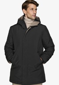 Cappotto imbottito nero con cappuccio, con fodera beige, zip frontale e due tasche laterali. Il tessuto appare liscio e isolato.