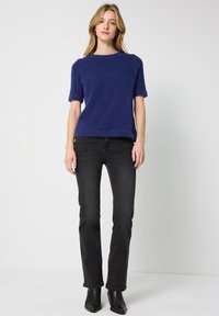 Mørkeblå kortærmet sweater lavet af blødt, tekstureret stof, parret med sorte slim-fit jeans og sorte ankelstøvler. Simpelt, rent design.