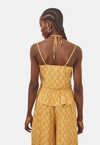 Top peplum amarillo con patrón floral, tirantes finos y detalle de lazo en la espalda. Presenta un dobladillo con volantes y una tela ligera para mayor comodidad.
