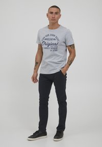 T-shirt di cotone grigia con testo grafico blu navy, dotata di scollatura rotonda e maniche corte, abbinata a pantaloni slim fit blu navy scuro e sneakers nere.