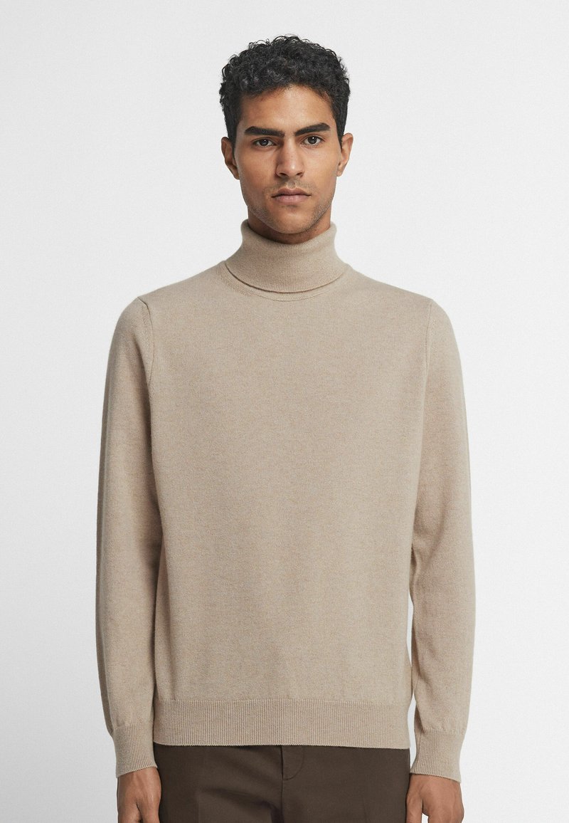Beige polokragejumper tillverkad av mjuk stickad tyg. Har långa ärmar och ribbad nederkant. Slät textur med minimal dekoration.