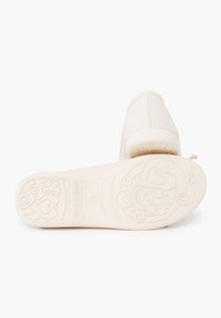 Chaussures beige avec une tige en tissu texturé. La semelle présente un motif floral et en cœur, fabriquées en Espagne. Design classique à enfiler.