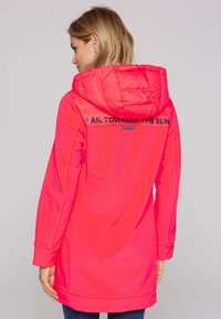 Pink waterproof jacket with a hood and elongated design. Features text "SAIL TOWARDS THE SUN" on the back and smooth, glossy texture.