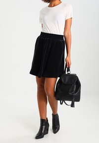 Svart sammetkjol med elastisk midja, tillsammans med en ljusgrå t-shirt. En svart läderryggsäck och ankelstövlar fulländar outfiten.