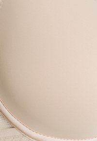 Soutien-gorge beige avec des bonnets lisses, un tissu doux et des coutures délicates. Présente une forme arrondie et des touches de dentelle sur les côtés.