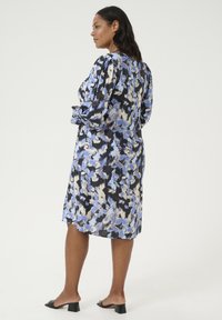 Vestido floral en negro, azul y crema con mangas abullonadas largas y un corte relajado. Presenta un escote redondeado y un dobladillo a la altura de la rodilla.