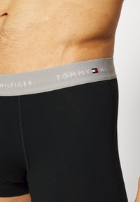 Schwarze Baumwollboxershorts mit einem grauen elastischen Bund, der das Logo "TOMMY HILFIGER" und einen kleinen farbigen Flaggenakzent zeigt.