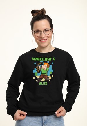 Czarna bluza z kapturem z pikselowym wizerunkiem postaci z Minecrafta, Alex, trzymającej łuk. Projekt zawiera zielone i niebieskie akcenty.