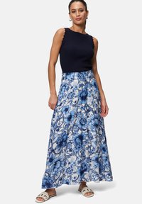 Débardeur côtelé bleu marine avec des bords festonnés associé à une jupe maxi florale dans des tons de bleu. Le modèle porte des sandales blanches à enfiler.
