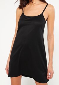 Svart ärmlös klänning med rak halsringning, tillverkad av mjukt tyg, med tunna axelband och lös passform.