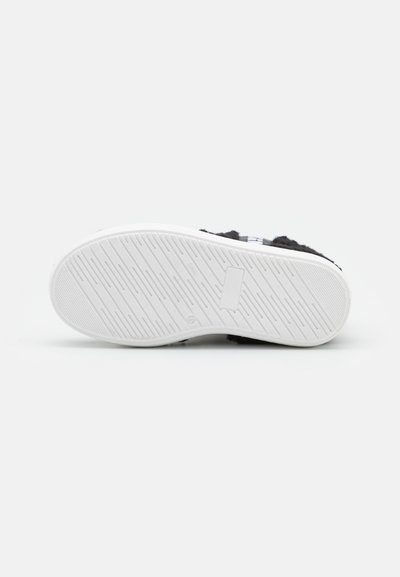 Sapatilha preta com um cabedal texturizado, sola de borracha branca com ranhuras horizontais e um logótipo estampado na lateral. Design minimalista.