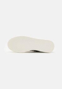 Semelle en caoutchouc blanc avec un motif de grip texturé, présentant une forme arrondie et une partie inférieure lisse pour une meilleure adhérence et durabilité.