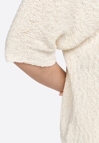 Helle, strukturierte Strickoberteil in Cremefarbe mit kurzen Ärmeln, das einen lockeren Sitz und ein offenes Strickmuster aufweist, ideal zum Darüberziehen und für die Freizeit.